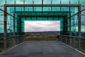 Grüne Glaskonstruktion auf einer Plattform. Blickt durch die offene Glassplitter ins Weserbergland