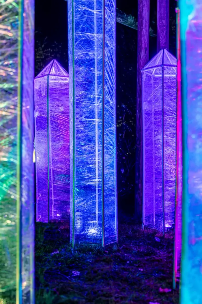 Beleuchtete, strukturierte Glastafeln in Blau- und Violetttönen, die bei Nacht im Freien aufgestellt werden.