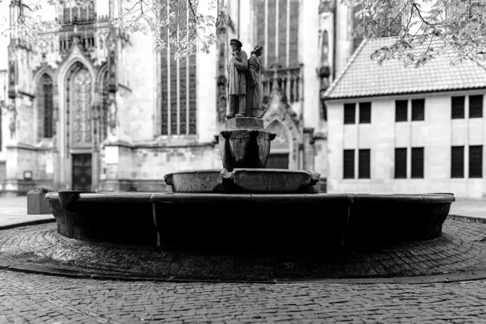 Ein Schwarz-Weiß-Bild eines Brunnens mit Statuen vor einer gotischen Kirche