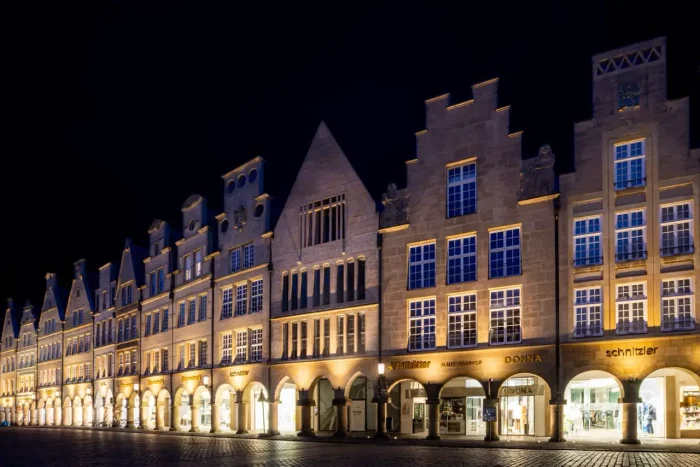 Eine Reihe historischer Gebäude mit beleuchteten Bögen im Erdgeschoss bei Nacht.