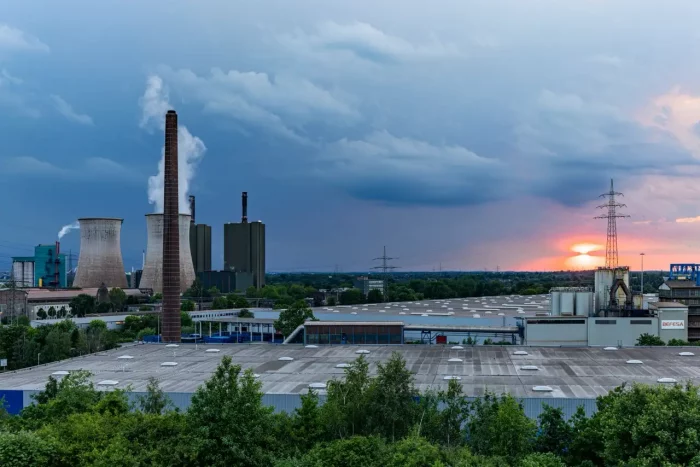 Industriekomplex mit großen Schornsteinen, die Dampf emittieren, vor dem Hintergrund von bewölktem Himmel und Sonnenuntergang.