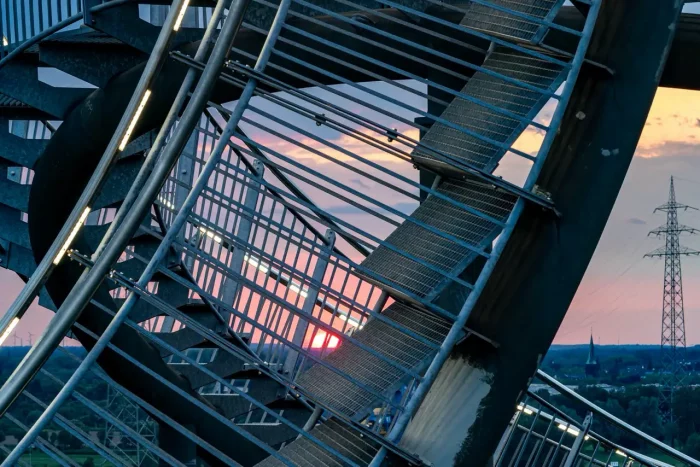 Metalltreppe mit einer komplexen Struktur, vor dem Hintergrund eines Sonnenuntergangs und Stromleitungen.
