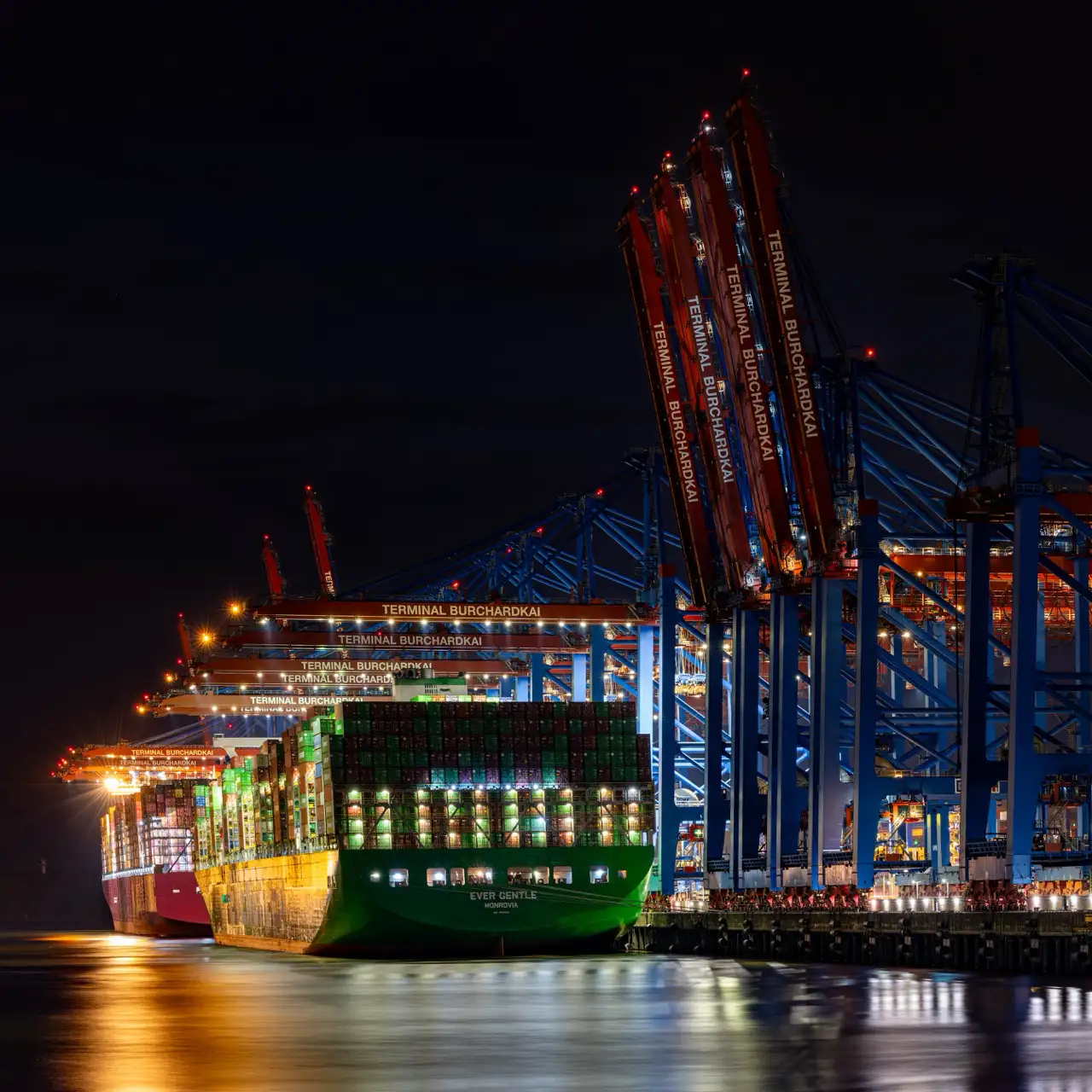Nachtansicht eines Containerschiffs, das am Terminal Burchardkai angedockt ist, mit Kränen und Lichtern, die das Gebiet beleuchten.