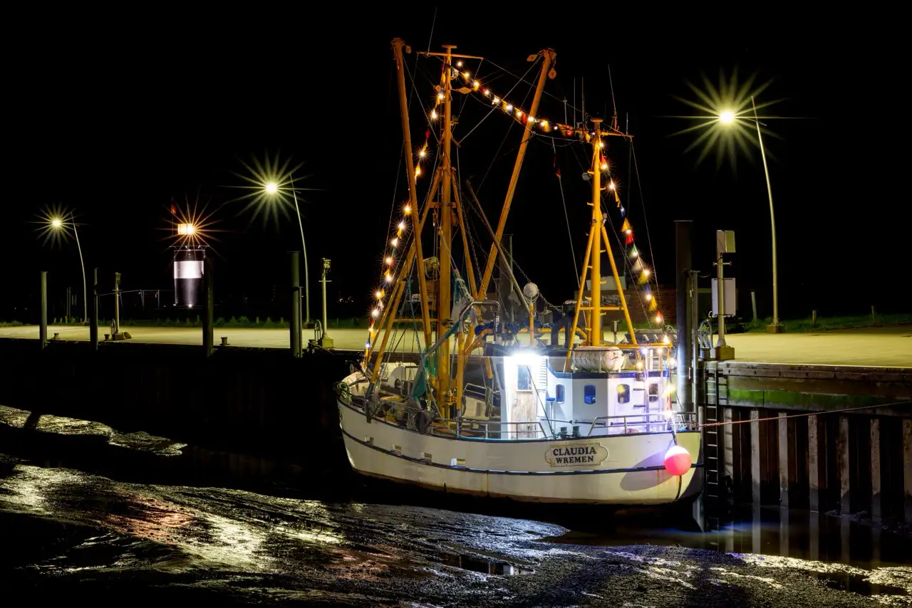 Fischerboote, die nachts angedockt sind und deren Lichter sich auf dem Wasser spiegeln.