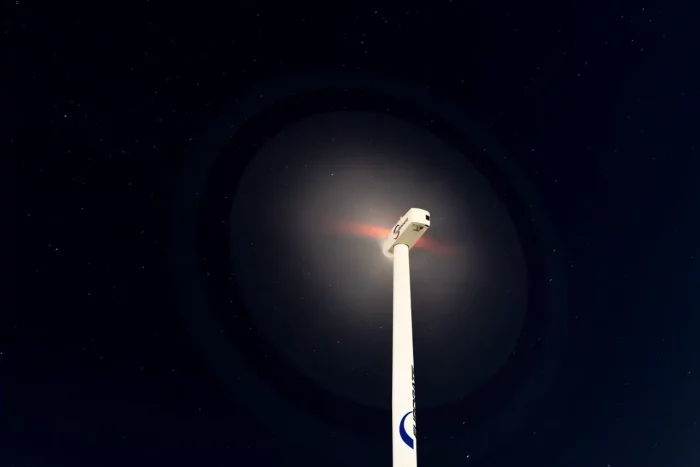 Windturbine vor einem sternenklaren Nachthimmel mit Lens-Flare-Effekt.