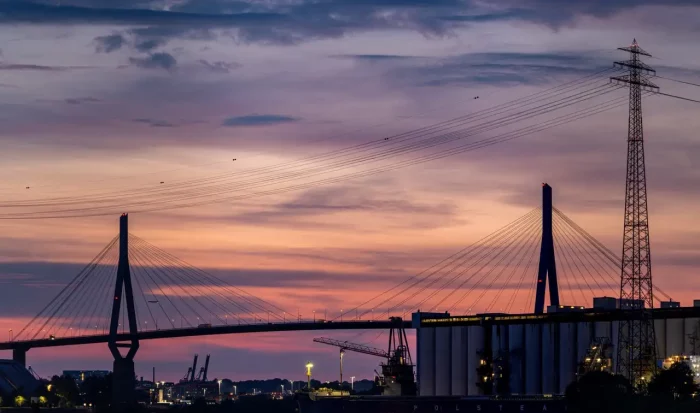 Silhouetten von Brücken- und Industriestrukturen vor einem farbigen Sonnenuntergangshimmel