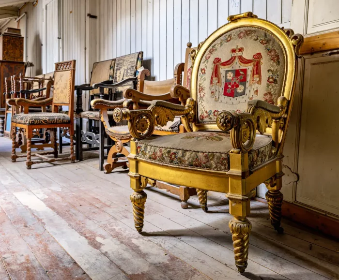 Eine Sammlung von verzierten Vintage-Stühlen, die in einer Reihe in einem Raum mit Holzböden und -wänden angeordnet sind.