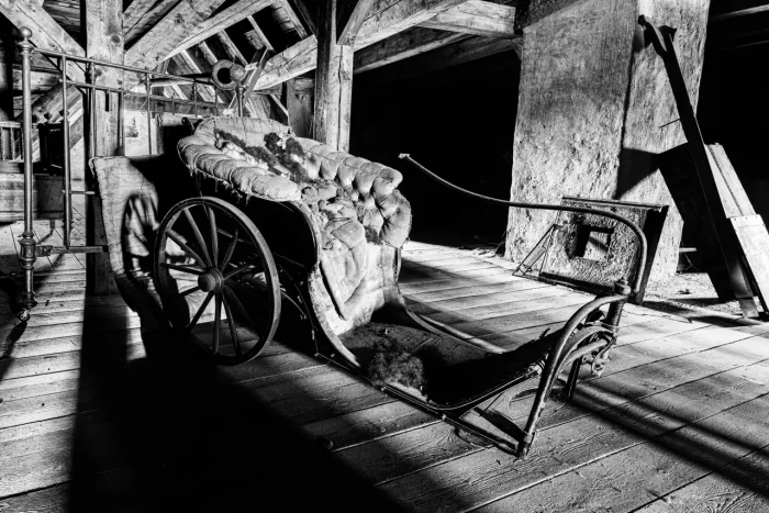 Schwarz-Weiß-Foto eines alten, verfallenen Wagens auf einem Dachboden mit Holzbalken und Boden.