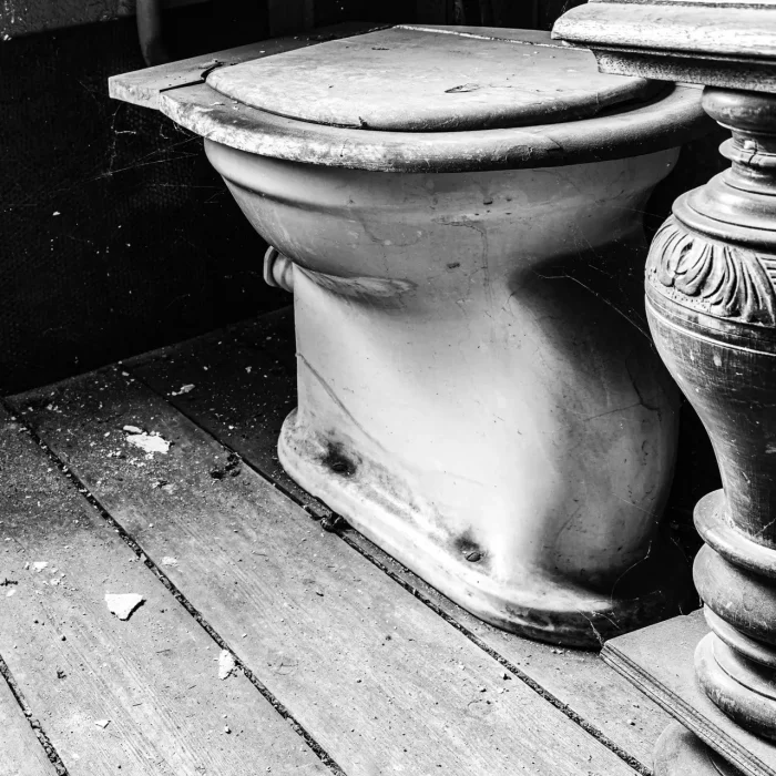 Eine alte, staubige Toilette mit Spinnweben in einem verlassenen Raum mit Holzboden.