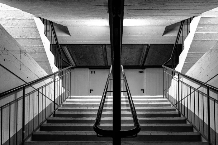 Schwarzweißfoto einer symmetrischen Betontreppe mit Geländern, die zu zwei weißen Türen führt
