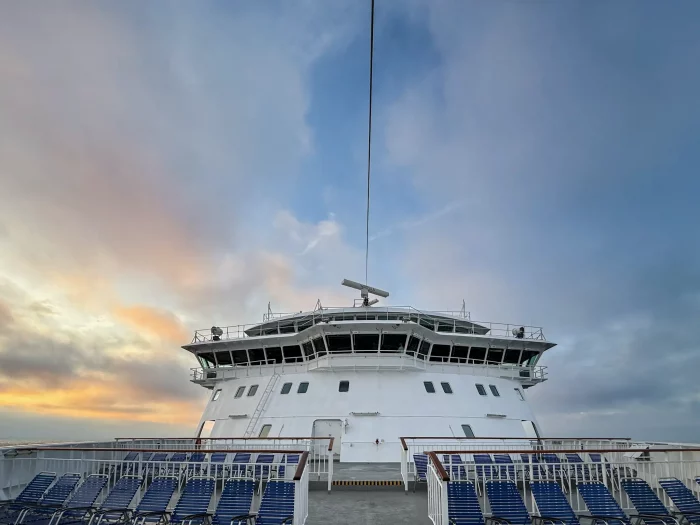 Brücke eines Schiffes mit Reihen leerer blauer Liegestühle unter bewölktem Himmel bei Sonnenuntergang