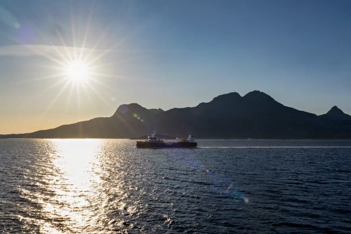 Sonnenuntergang über einem ruhigen Meer mit einem Frachtschiff vor einer Bergsilhouette