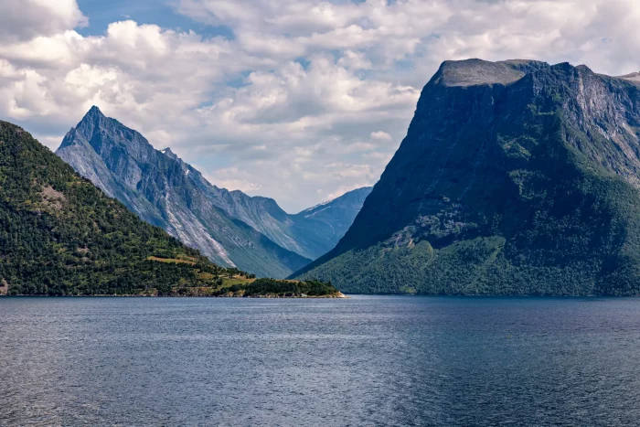 Hjørundfjorden mit steilen bewaldeten Bergen und ruhigem Wasser unter bewölktem Himmel