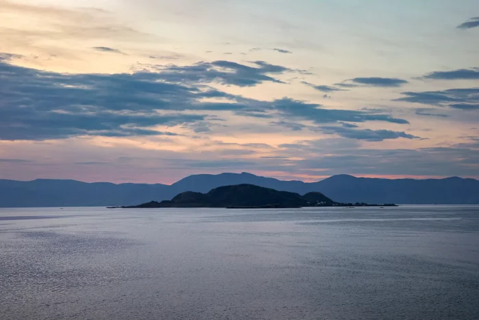 Meer mit Inseln und Bergen im Hintergrund unter bewölktem Himmel bei Sonnenuntergang