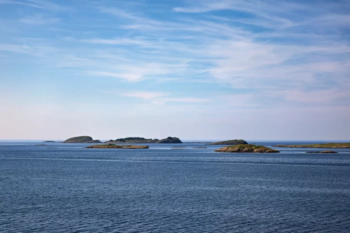 Mehrere kleine Inseln im ruhigen Meer unter blauem Himmel mit leichter Bewölkung