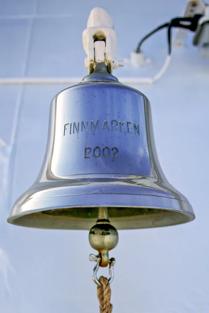 Schiffsglocke mit der Gravur 'FINNMARKEN 2002', aufgehängt an einer weißen Halterung