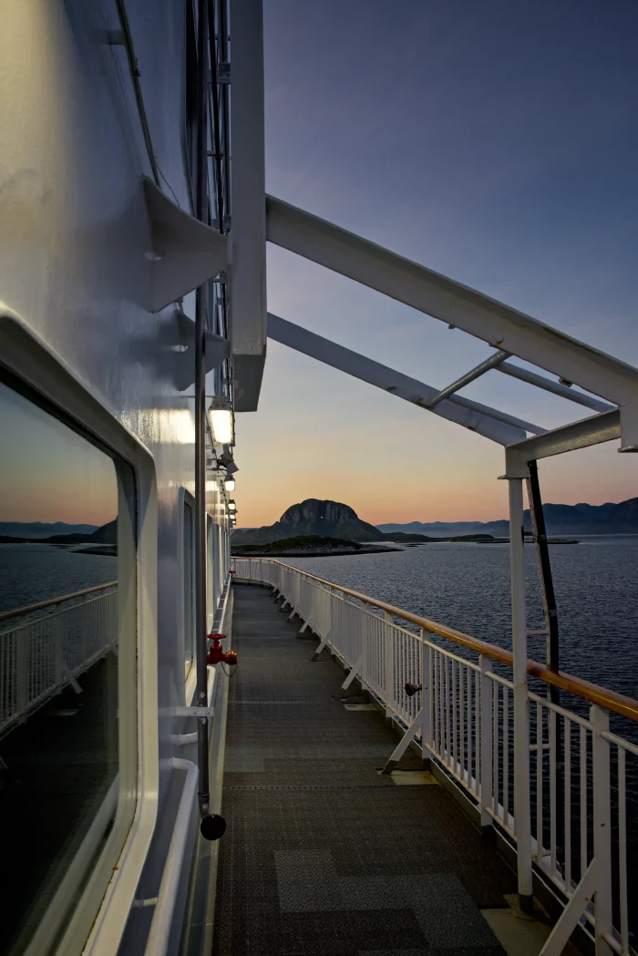 Blick vom Deck eines Hurtigruten-Schiffs auf das Meer und eine Felseninsel bei Sonnenuntergang
