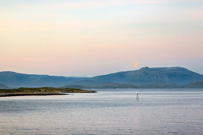 Blick auf ruhiges Meer mit kleinen Inseln und Bergen im Hintergrund bei Sonnenuntergang