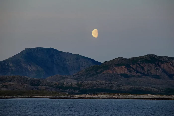 Halbmond über zerklüfteten Bergen am Meer bei Dämmerung