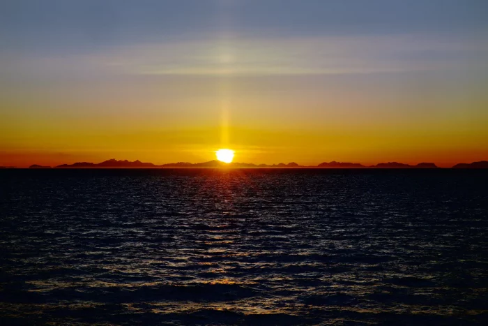 Sonnenuntergang über dem Meer mit dunklen Bergen am Horizont