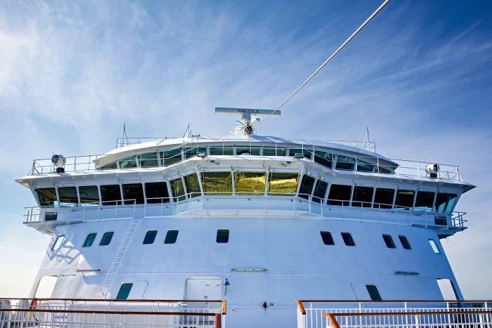 Vorderansicht eines weißen Kreuzfahrtschiffs mit Brücke und Antennen unter blauem Himmel
