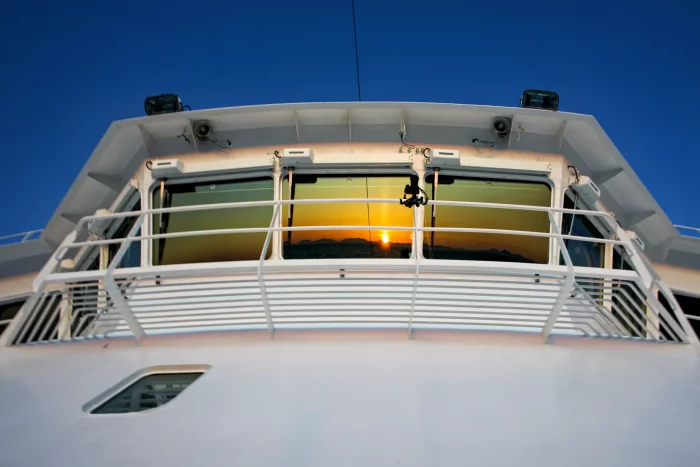 Sonnenuntergang spiegelt sich in den Fenstern der Brücke eines Hurtigruten-Schiffs