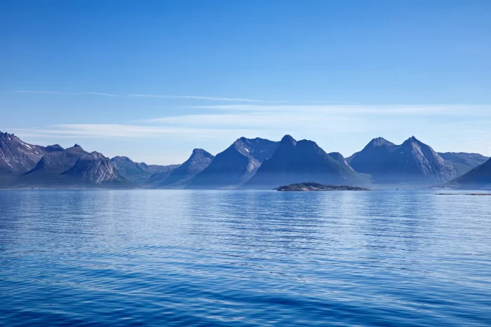 Berglandschaft mit mehreren Gipfeln und Inseln im ruhigen Meer unter klarem Himmel