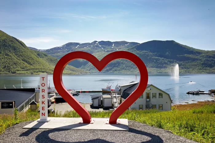 Rotes Herzskulptur mit Blick auf Fjord, Berge und Wasserfontäne in Torsken, Norwegen