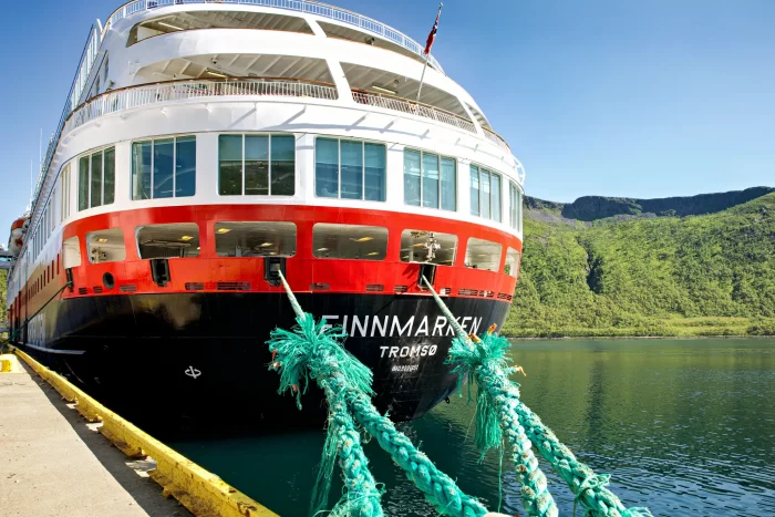 Vorderansicht des Hurtigruten-Schiffs 'Finnmarken' in Tromsø, festgemacht mit dicken grünen Taue an einem Kai, umgeben von Wasser und Bergen
