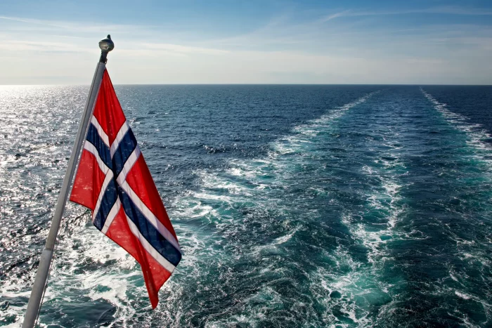 Norwegische Flagge weht am Heck eines Schiffes auf offenem Meer mit sichtbarer Schiffsspur