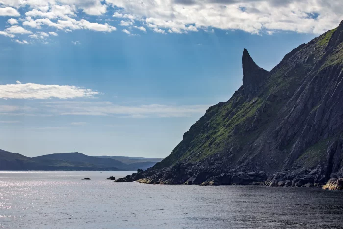 Felsige Küste mit steilem, spitz zulaufendem Berg unter bewölktem Himmel am Meer