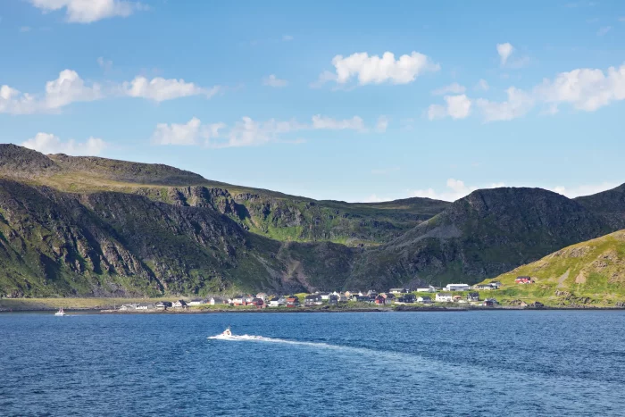 Kleines Boot fährt auf ruhigem Meer vor einer Küste mit grünen Hügeln und einem kleinen Dorf