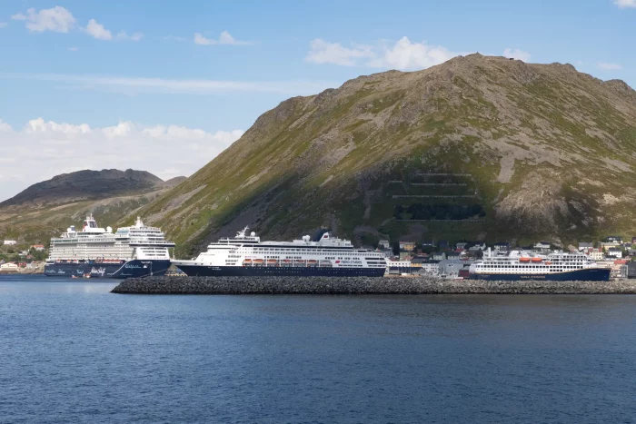 Drei Kreuzfahrtschiffe liegen im Hafen vor einem großen Berg unter blauem Himmel