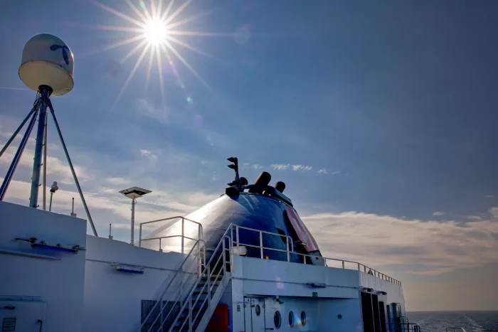Sonniger Himmel über dem Deck eines Hurtigruten-Schiffs mit sichtbaren Antennen und Treppenaufgang
