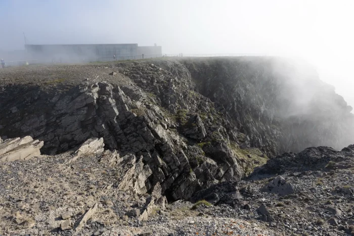 Felsige Klippen am Nordkap mit Nebel und einem Gebäude im Hintergrund