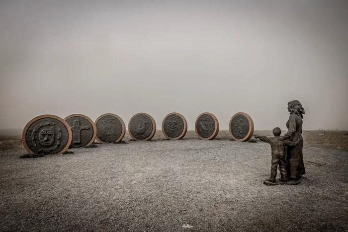 Skulptur am Nordkap mit sieben großen runden Reliefs und zwei Figuren, einer Frau und einem Kind, die auf die Reliefs blicken
