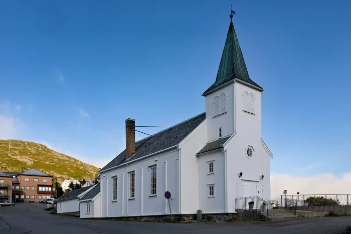Weiße Kirche mit grünem Turm und Wetterfahne vor blauem Himmel in einer kleinen Stadt