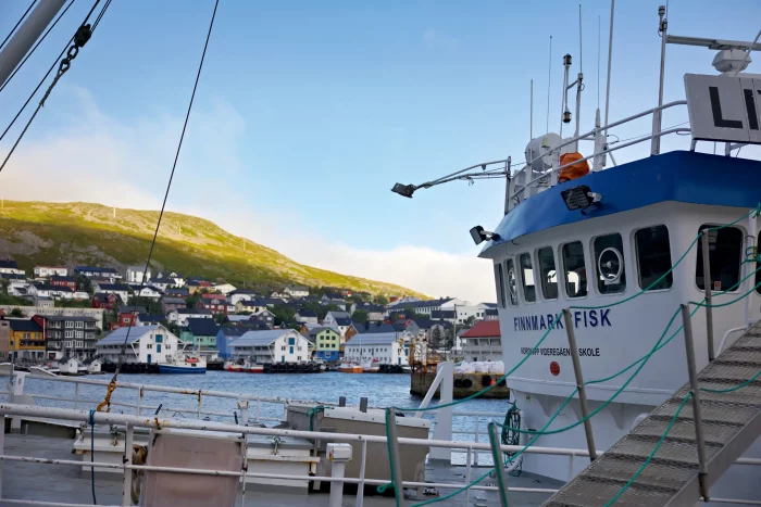 Fischereischiff 'Finnmark Fisk' am Hafen mit Blick auf Häuser und grüne Hügel im Hintergrund