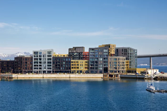 Moderne mehrstöckige Wohngebäude am Wasser mit Segelboot im Hafen und schneebedeckten Bergen im Hintergrund