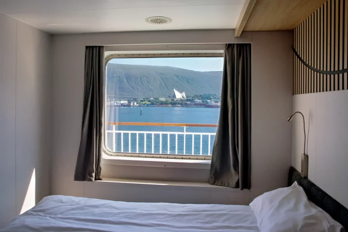 Blick aus einer Kabine auf einem Schiff auf Fjord mit Bergen und markanter weißer Architektur am Ufer