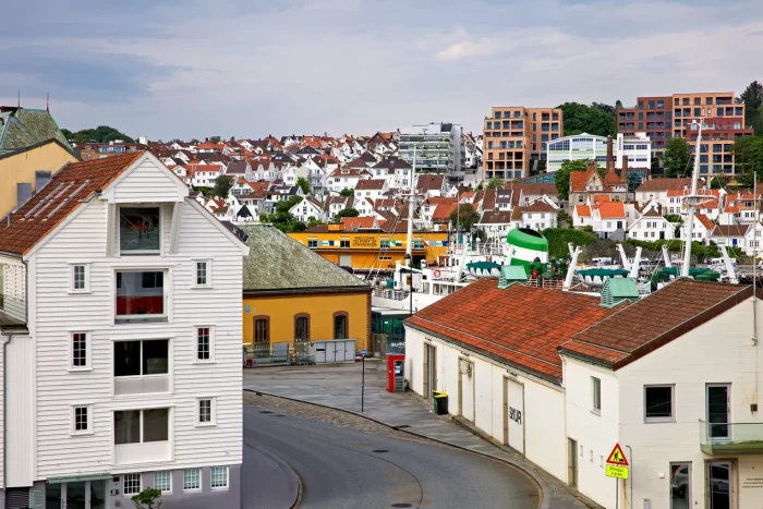 Blick auf Hafen mit weißen Booten und gelbem Hurtigruten-Schiff vor Stadt mit weißen und roten Häusern und modernen Gebäuden