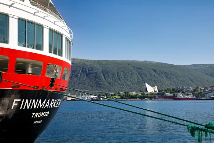 Bug des Hurtigruten-Schiffs 'Finnmarken' im Hafen von Tromsø mit Blick auf Wasser und bewaldete Berge