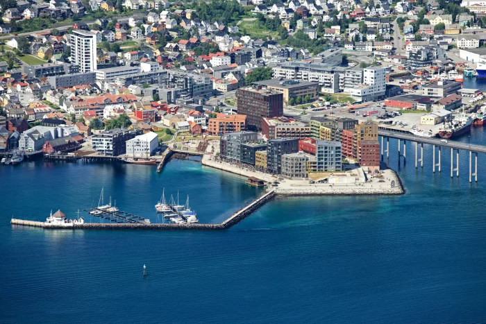Hafen mit mehreren modernen Gebäuden am Wasser und einem angelegten Hurtigruten-Schiff in einer norwegischen Stadt