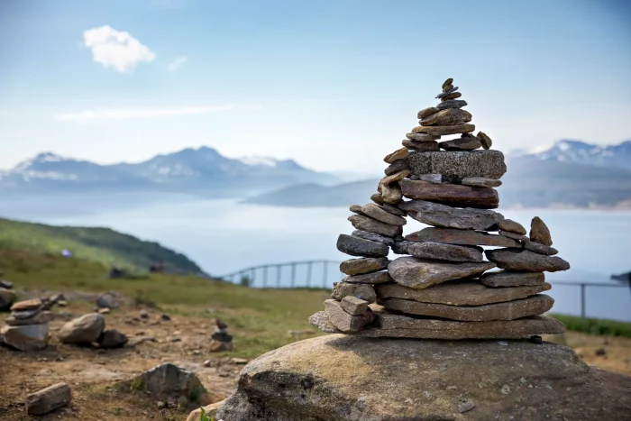 Gestapelte Steine auf einem Felsen mit Blick auf Fjord und Berge im Hintergrund
