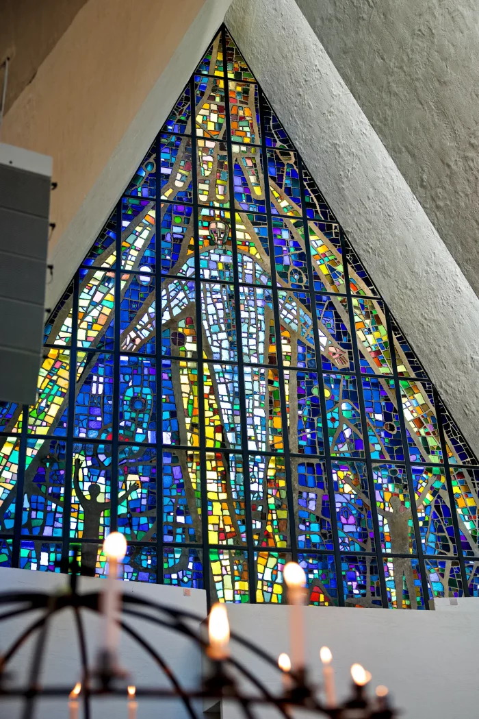 Dreieckiges Buntglasfenster mit abstraktem Muster in Blau-, Gelb- und Grüntönen in einer Kirche