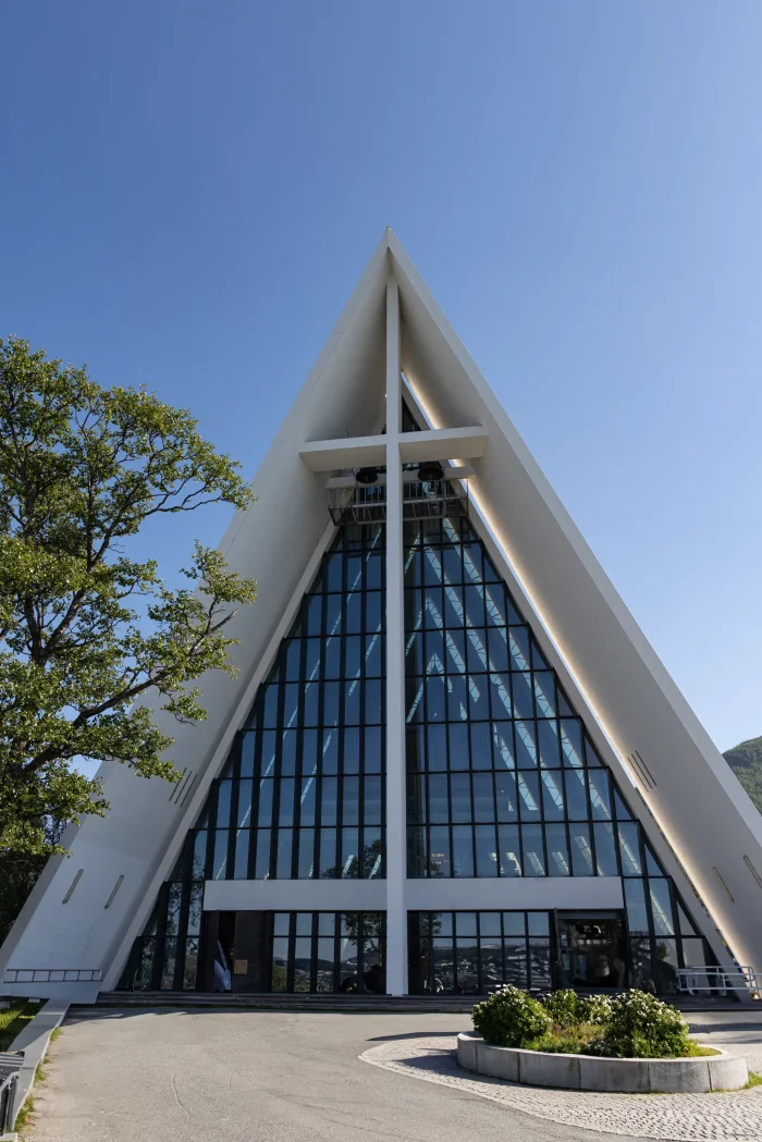 Moderne Kirche mit spitzem A-förmigem Dach und großem Glasfenster, umgeben von Bäumen und blauem Himmel