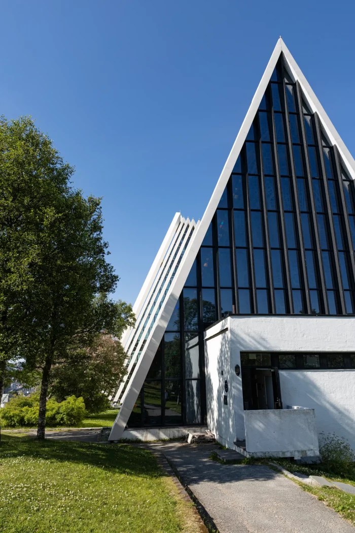 Dreieckiges modernes Gebäude mit großen Glasfenstern und weißer Fassade neben einem Baum unter blauem Himmel