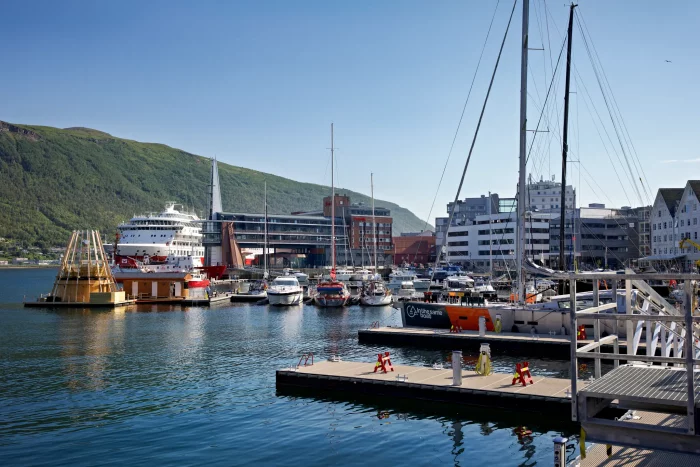 Hafen mit mehreren Booten und Schiffen, im Hintergrund grüne Hügel und moderne Gebäude