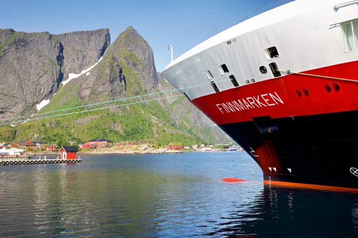 Bug des Hurtigruten-Schiffs 'Finnmarken' vor einer norwegischen Fjordlandschaft mit Bergen und roten Häusern