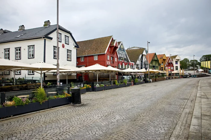 Reihe bunter Holzhäuser mit Cafés und Restaurants entlang einer gepflasterten Straße in einer norwegischen Hafenstadt